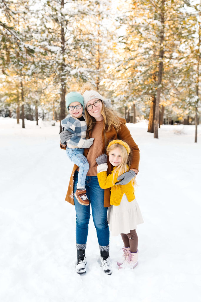 blonde mother and two children sitting smiling and standing in the snow during winter family photoshoot