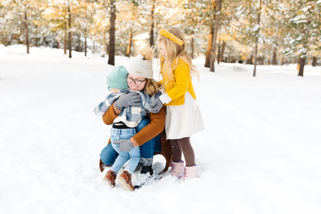 blonde mother and two children hugging in the snow during winter family photoshoot
