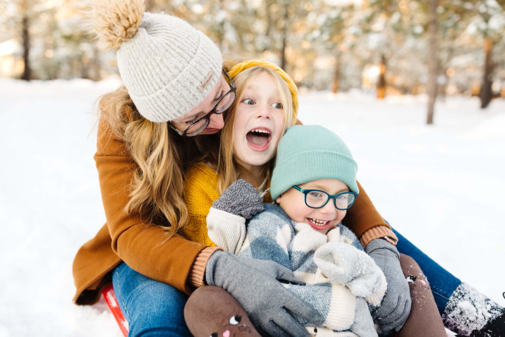 mother snuggling up and tickling children in the snow during winter family photoshoot