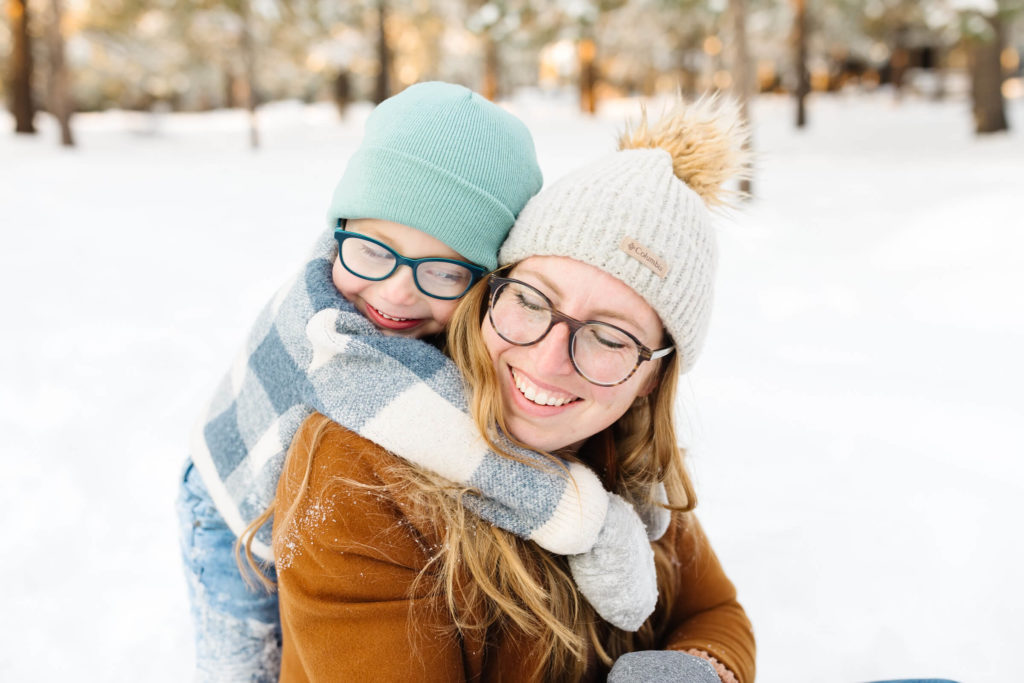 little boy in blue plaid sweater hugging mother in brown jacket during winter family photoshoot