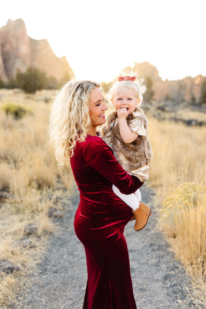 pregnant blonde mother holding little blonde girl with bow in her hair during maternity family photoshoot