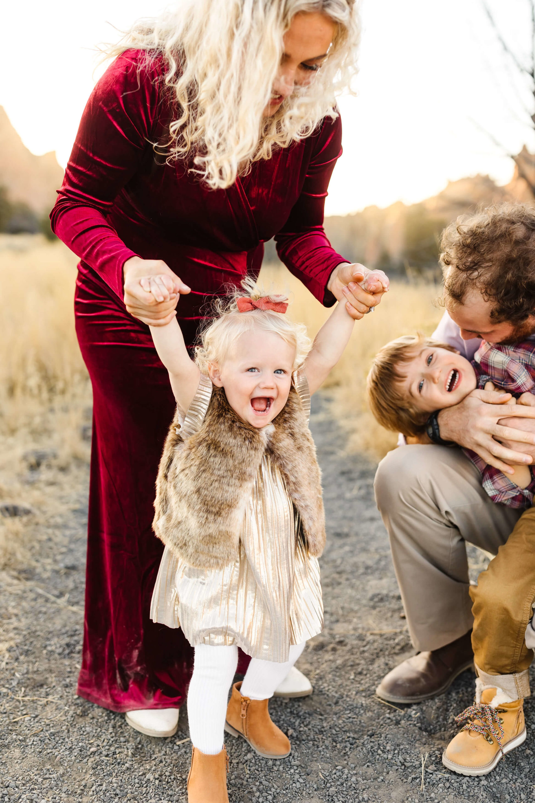 blonde mother in red velvet dress holding little blond girl while she laughs during maternity family photoshoot