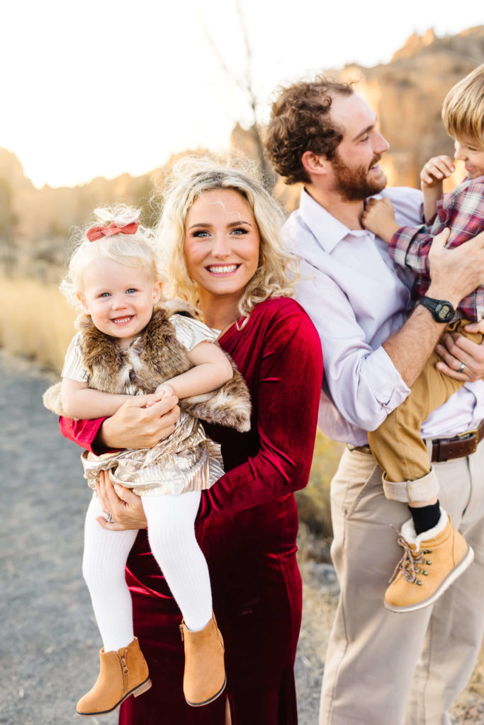 pregnant blonde mother holding little blonde girl wearing fur vest at smith rock during maternity family photoshoot