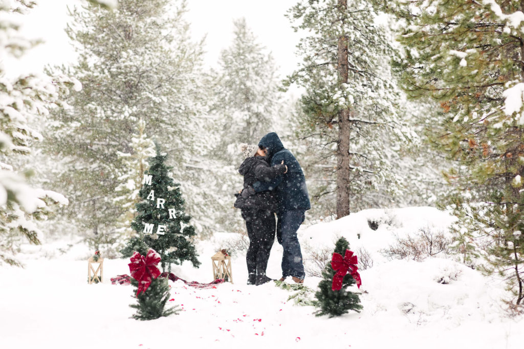 man and woman in snow embracing after surprise christmas proposal