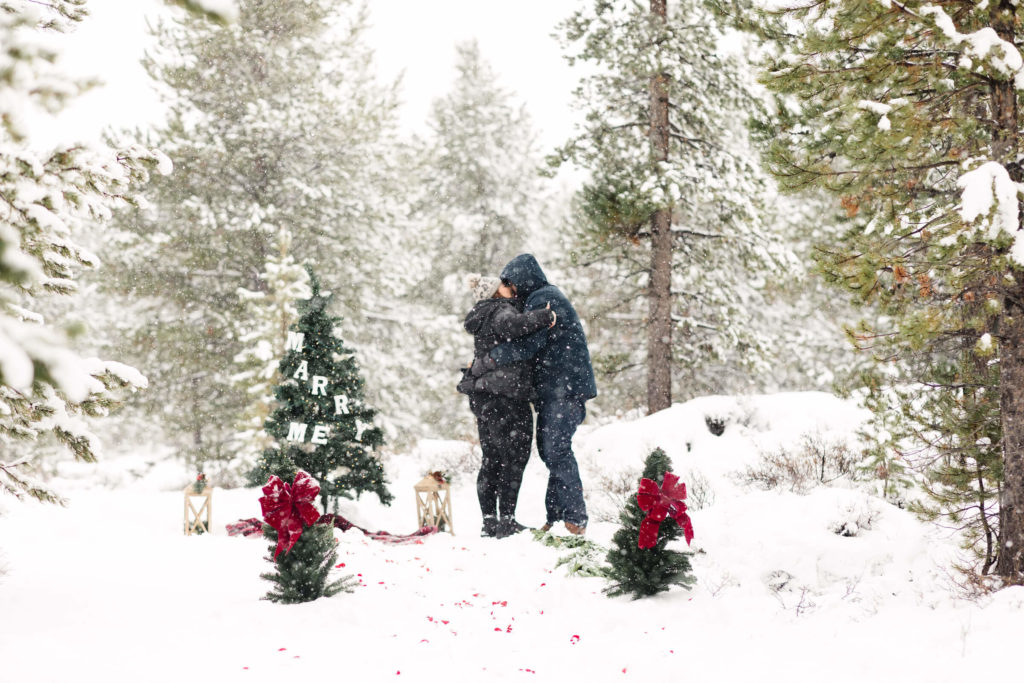 man and woman kissing during surprise proposal in the snow 