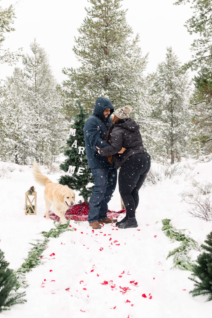 man and woman laugh and celebrate in snow after surprise christmas proposal