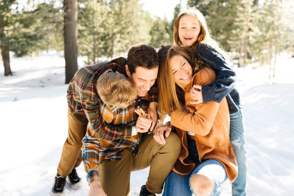 two children hugging their parents from behind while in the snow during family photo session at mt. bachelor