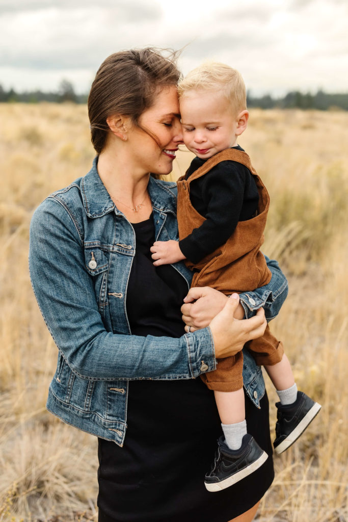 brunette mother nuzzling cheek of blonde little boy in brown overalls during discussion of cost of family photography