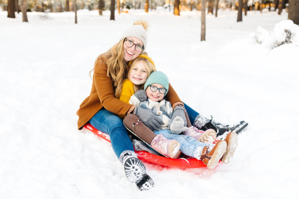 blonde mother sitting on red sled with two children during family photo session