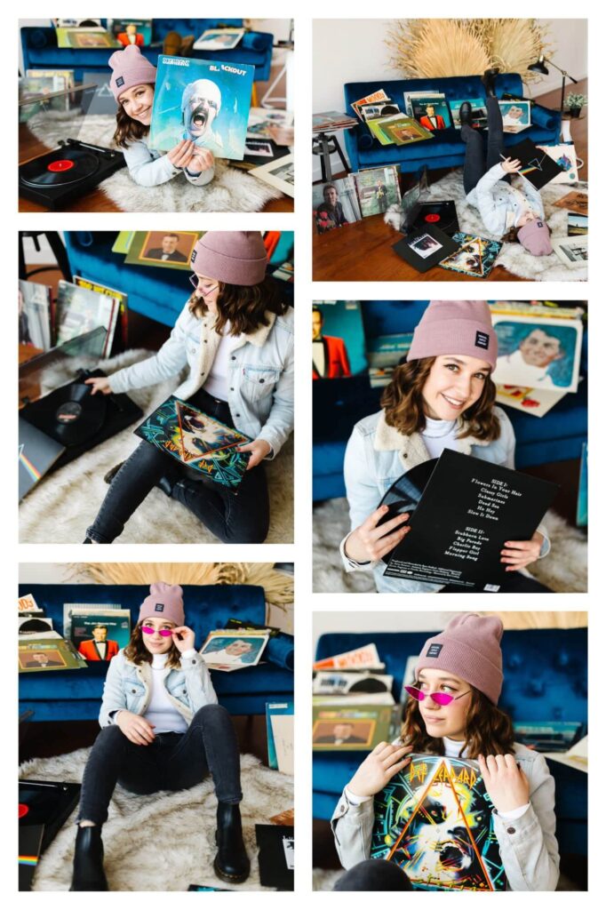brunette young high school senior girl wearing jean jacket and pink beanie sitting in front of blue velvet couch with records and record player during unique vintage record themed senior photo session