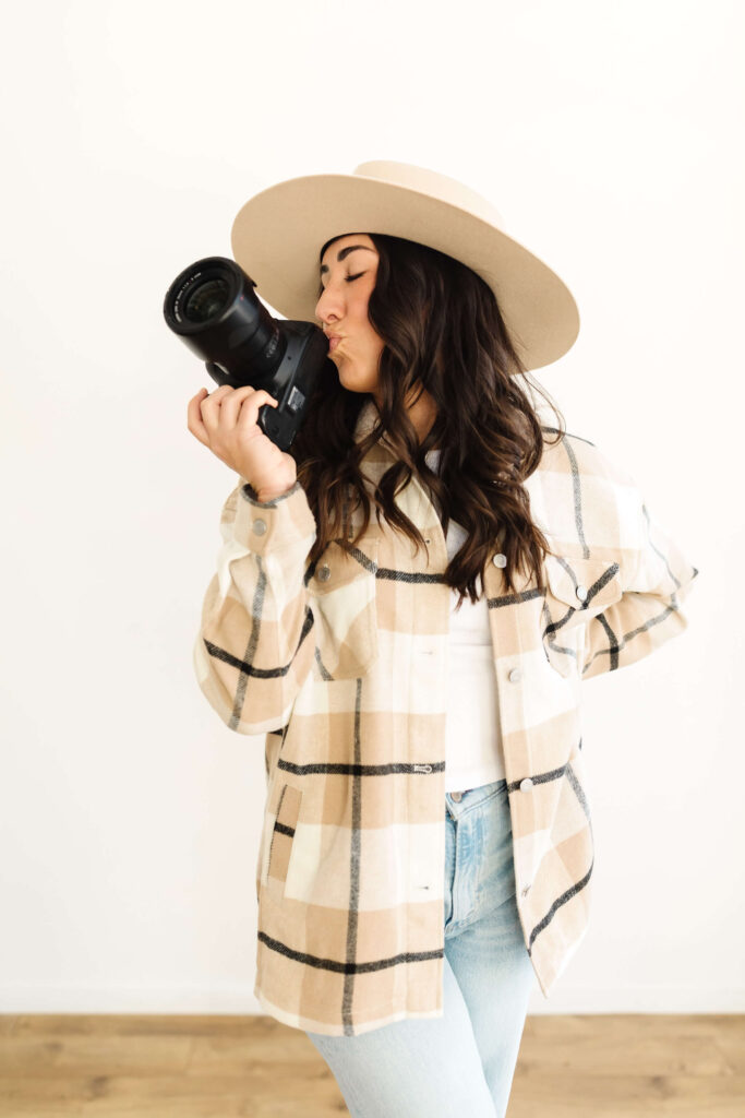 woman in wide brimmed hat standing  kidding her canon camera during creative poses photographers headshots session