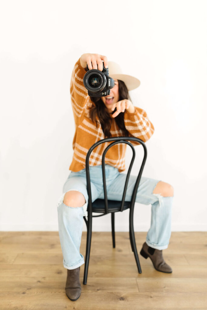 canon camera being held out in front of woman sitting backwards in a chair during poses for creative photographers headshots session