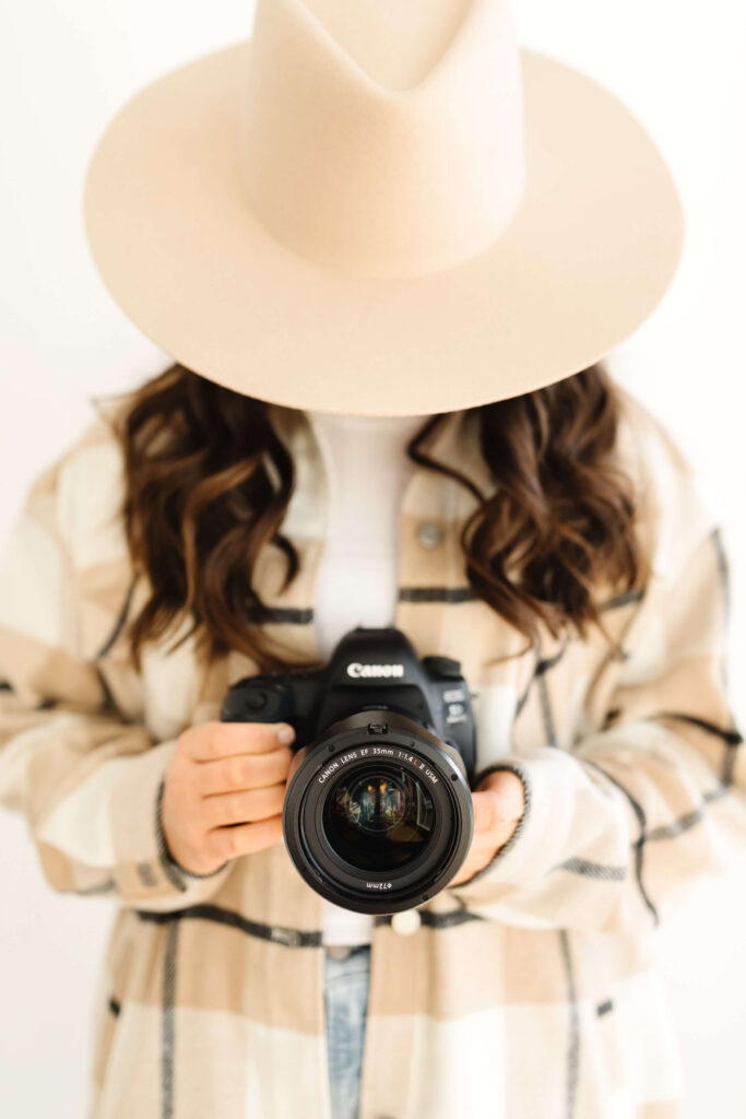 brunette in wide brimmed felt hat holding camera in front of her body during poses for creative photographers headshots session