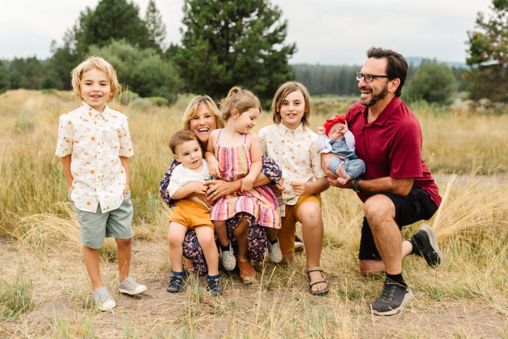 grandparents kneel in tall grass with 5 grandchildren for photographer during Sunriver family photo session along deschutes