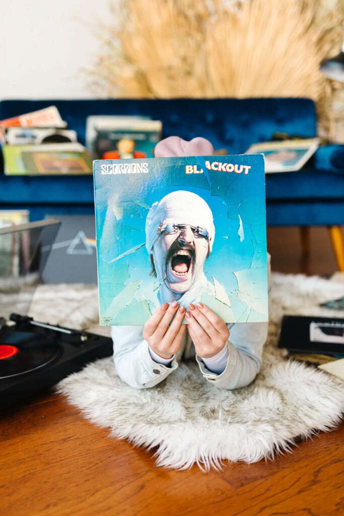 girl laying in front of blue velvet couch with scorpions blackout vinyl record album held in front of her face during senior studio photoshoot