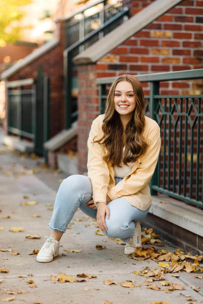 a girl in a yellow shacket sitting on cement staircase next to brick buildings during golden hour senior photos 